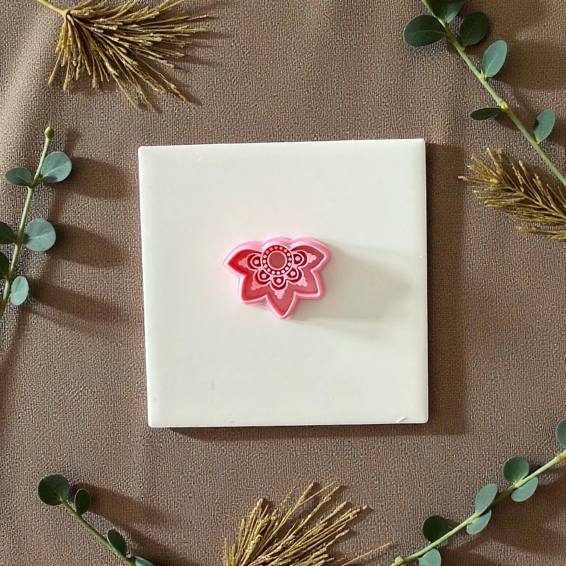 Pink lotus mandala clay cutter centered on white tile with beige cloth