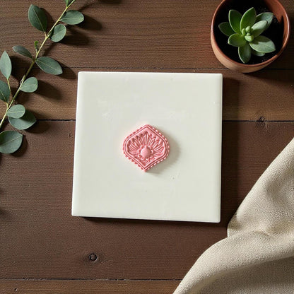 Diamond floral clay imprint centered on white tile with eucalyptus and neutral backdrop
