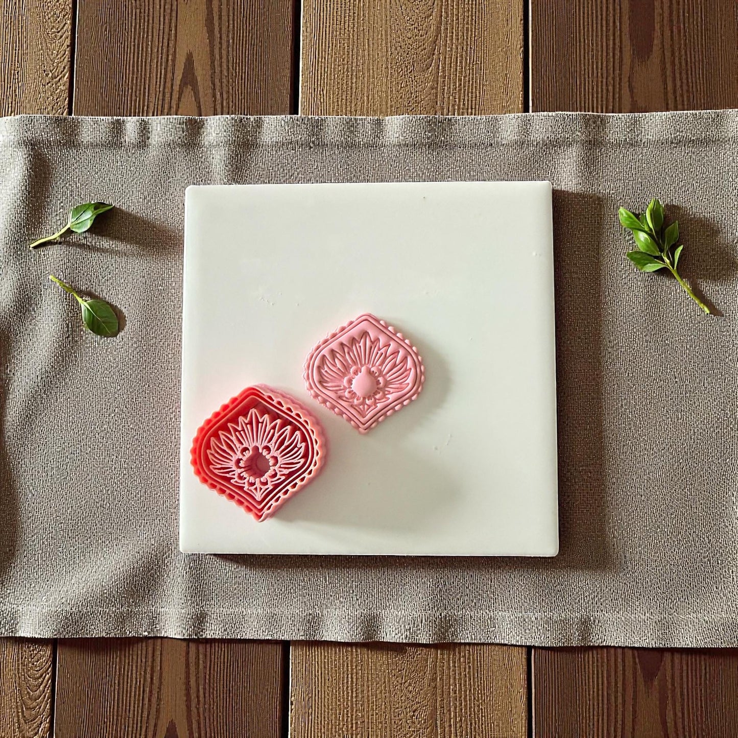 Pink diamond sunburst clay cutter beside imprint on white tile surrounded by greenery
