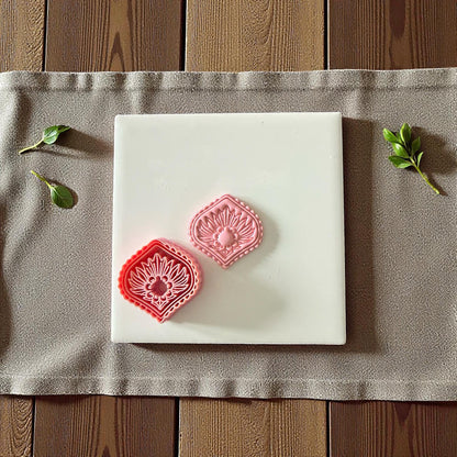 Pink diamond sunburst clay cutter beside imprint on white tile surrounded by greenery
