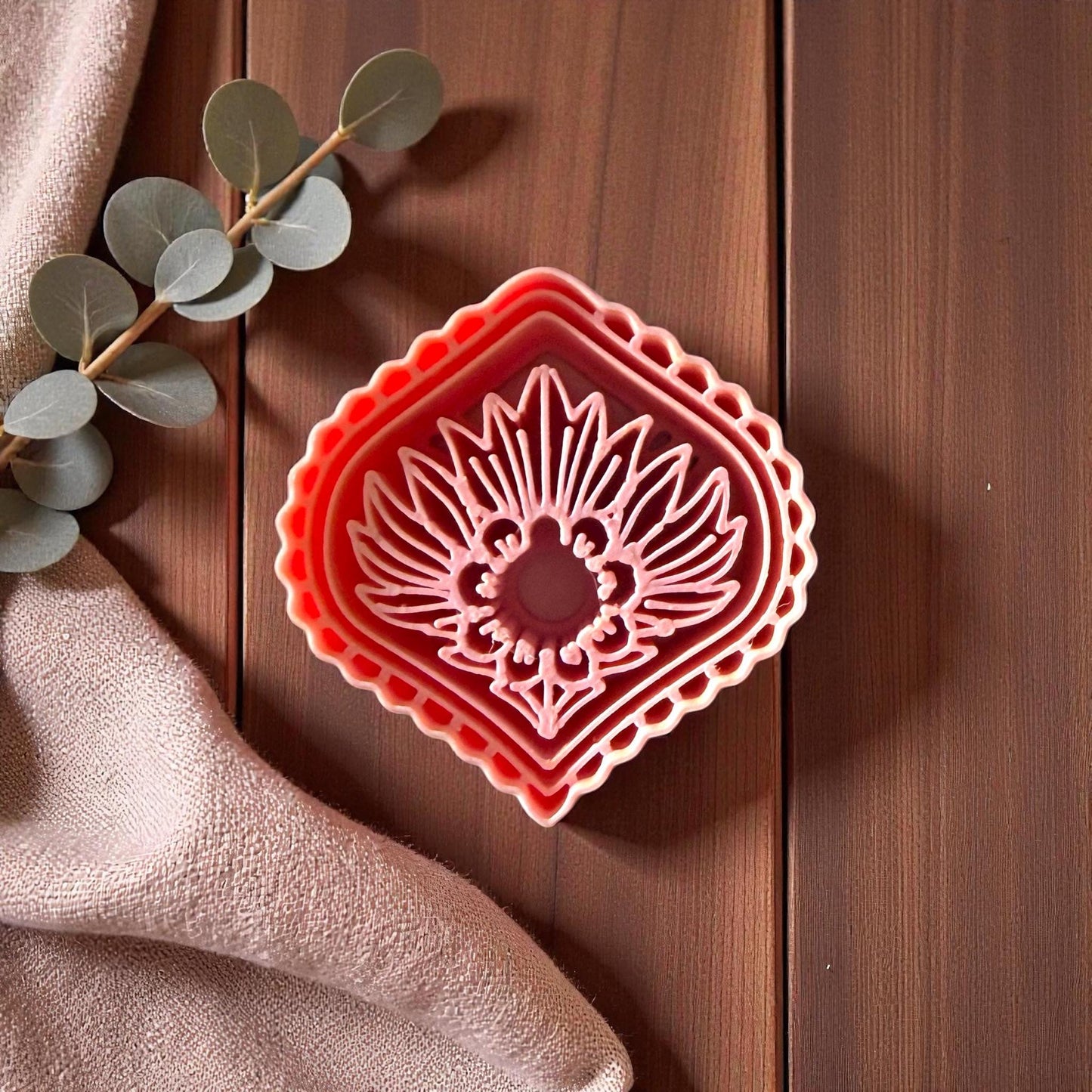 Pink diamond sunburst polymer clay cutter on wooden background with beige fabric and eucalyptus