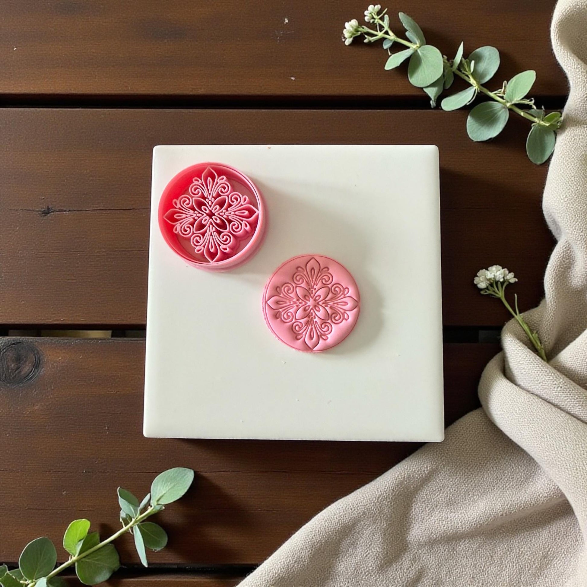 Floral mandala clay cutter and imprint displayed on white tile with greenery