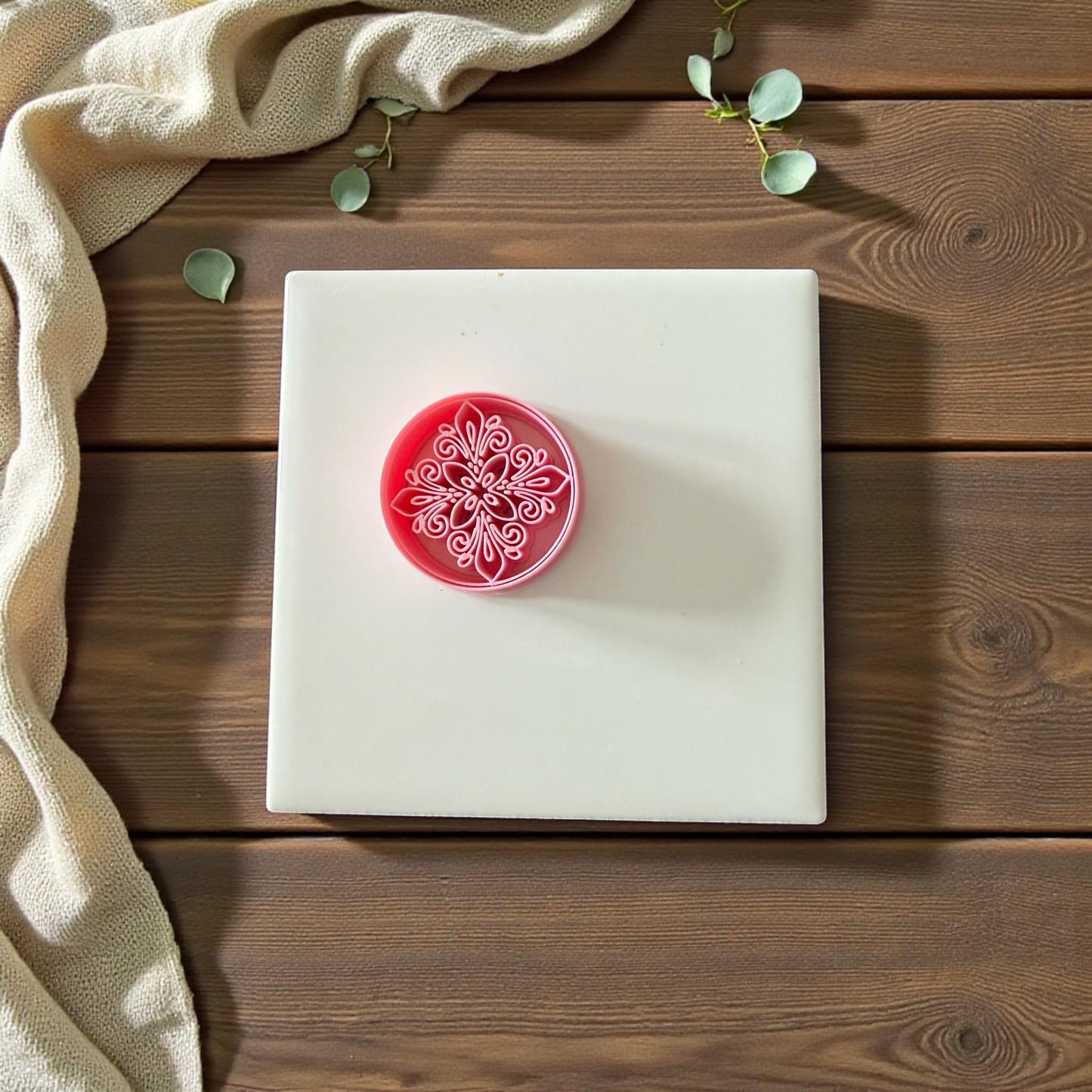 Pink circular mandala clay cutter centered on white tile with neutral cloth