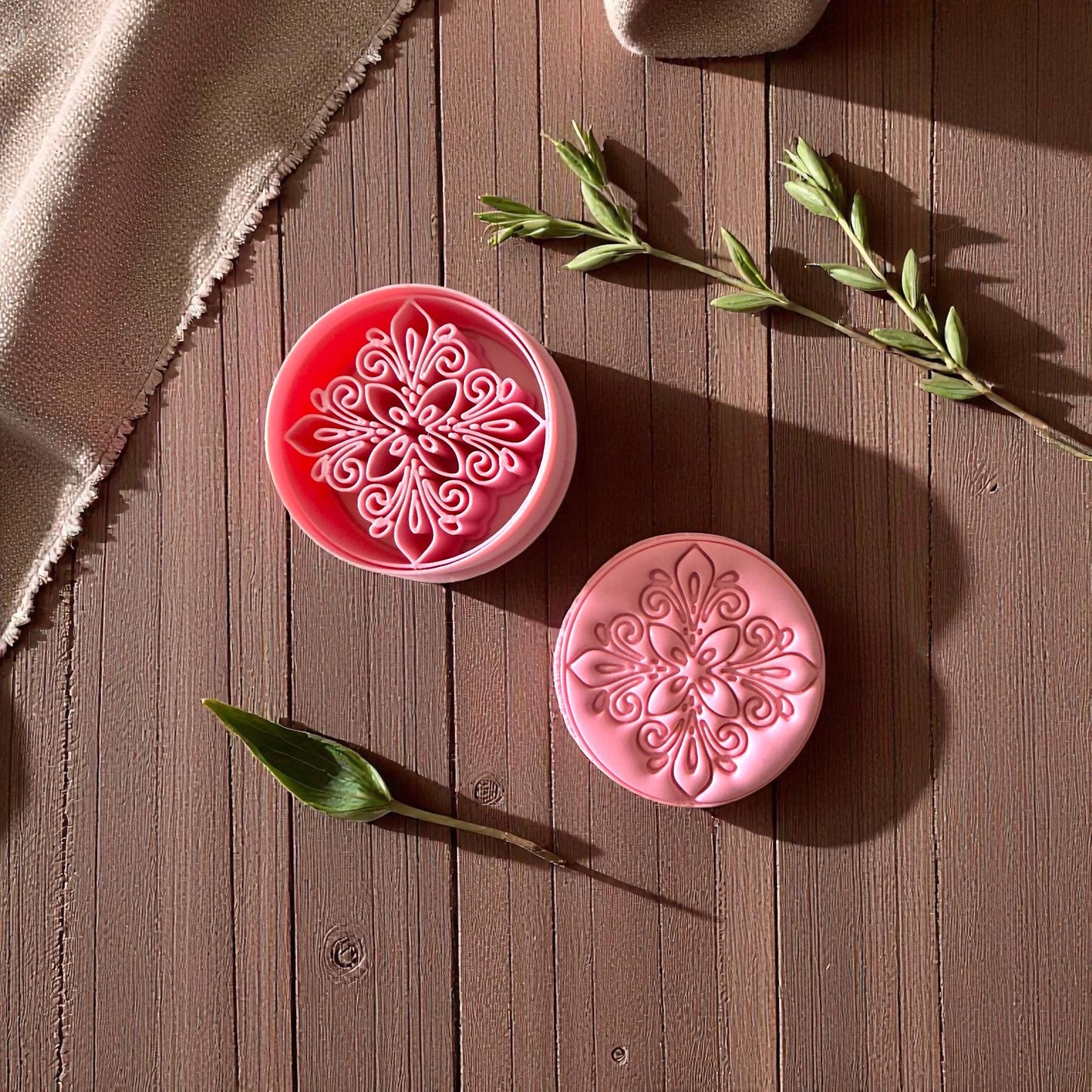 Two pink round clay cutters with ornate boho design on brown wood background