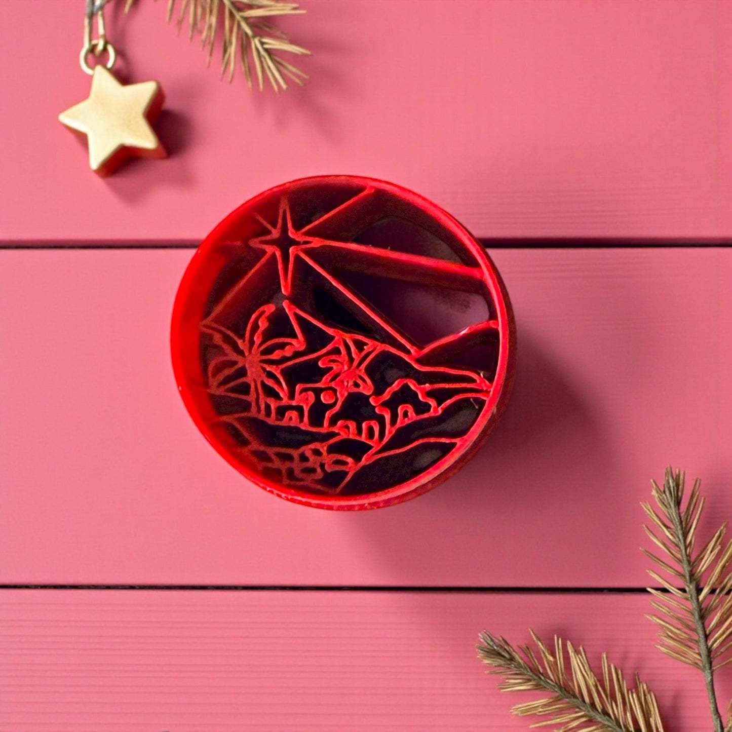 Red Bethlehem clay cutter on pink wood background with pine and star decor