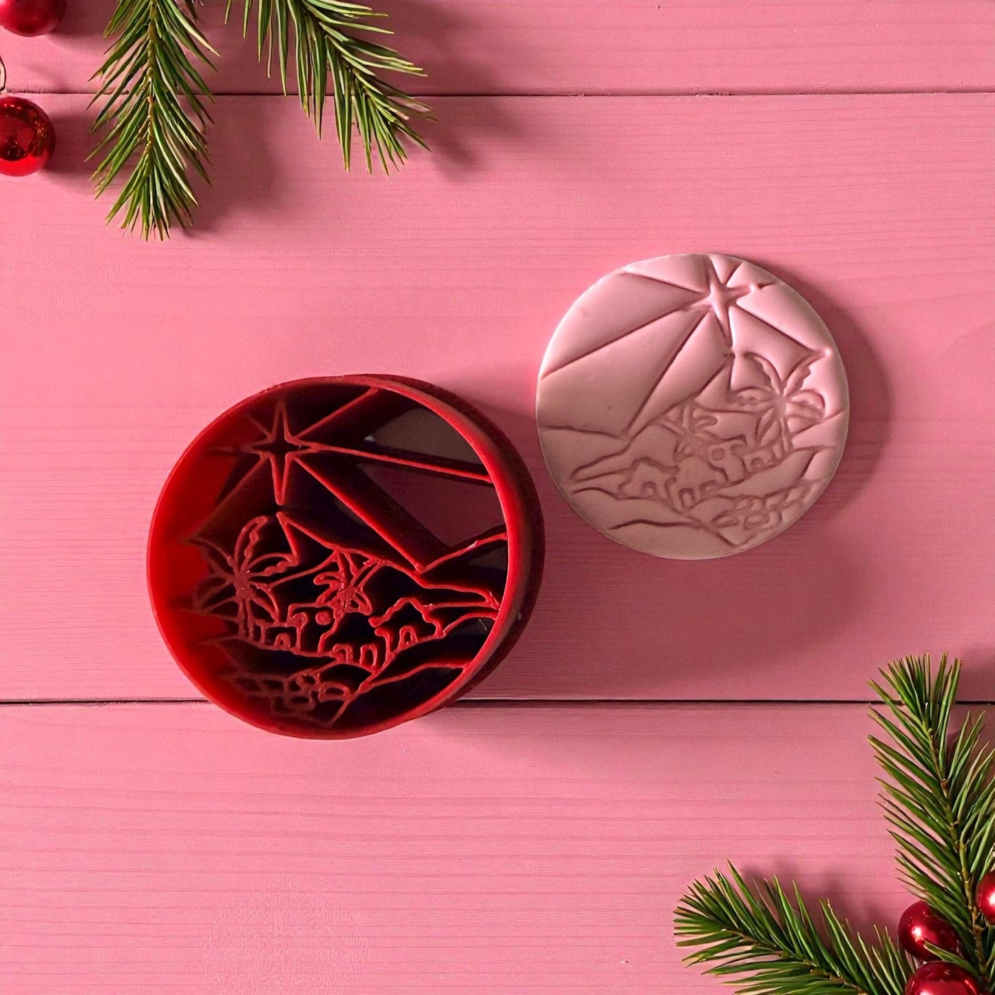 Red polymer clay cutter with Bethlehem nativity scene beside pink clay imprint