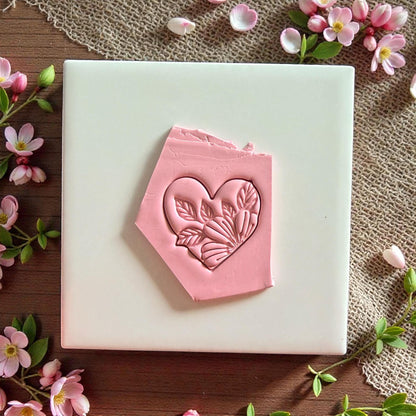 Pink clay heart impression in clay slab surrounded by flowers and leaves