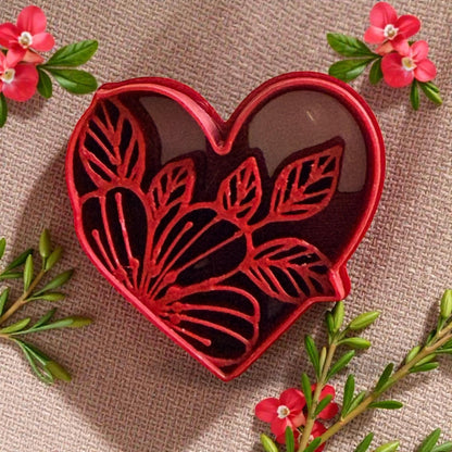 Red heart-shaped cutter with floral leaf design surrounded by pink flowers and greenery