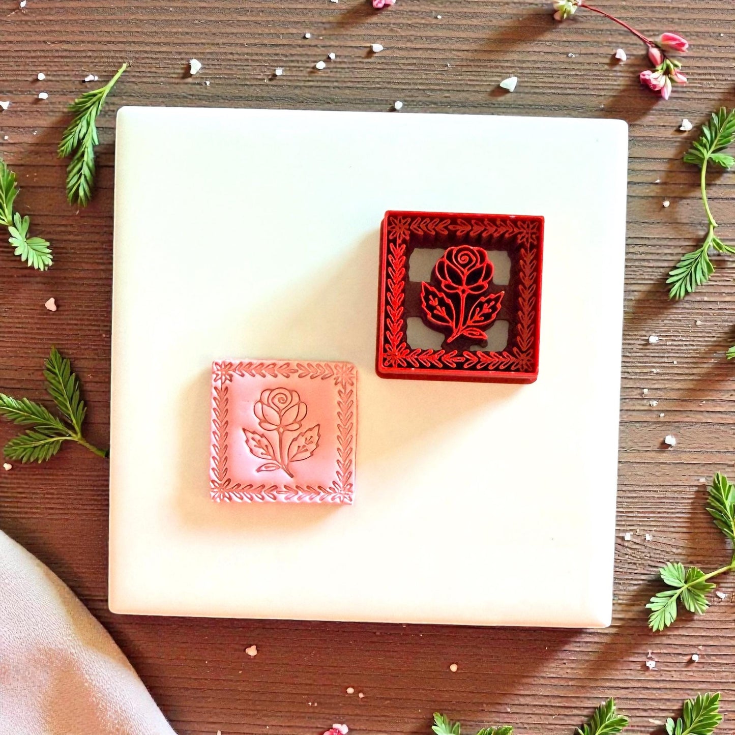 Red floral cutter and pink clay rose square displayed on white tile with greenery