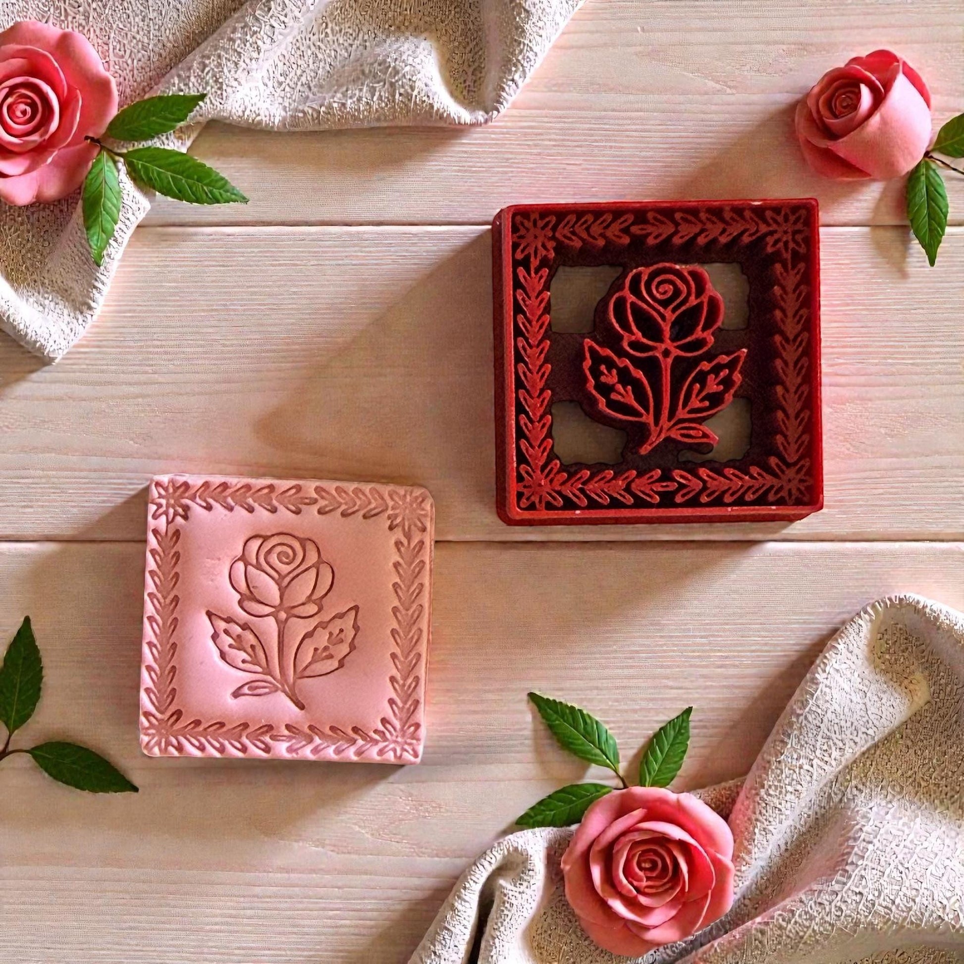 Red rose frame cutter beside pink clay impression surrounded by roses and fabric