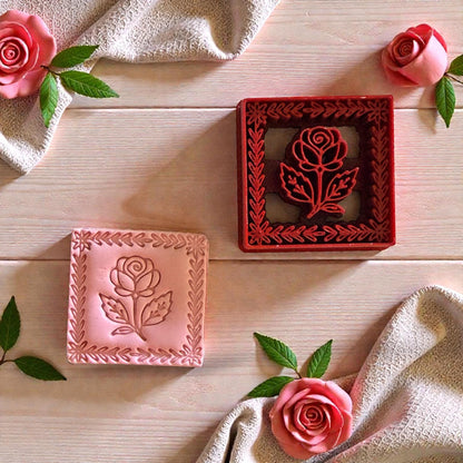 Red rose frame cutter beside pink clay impression surrounded by roses and fabric