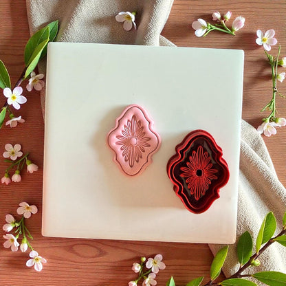 Red floral cutter and pink clay impression on white tile with flowers and leaves