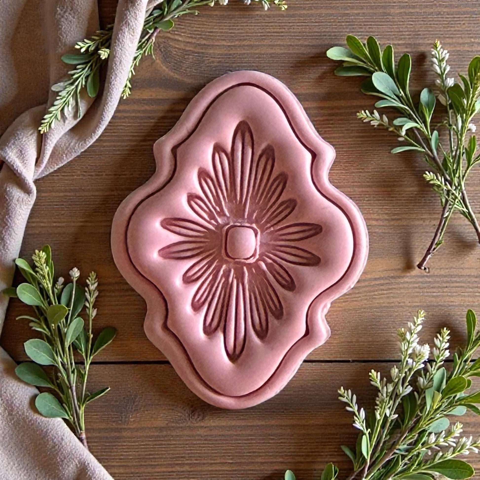 Pink clay floral medallion with ornate border and green foliage around