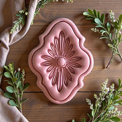 Pink clay floral medallion with ornate border and green foliage around