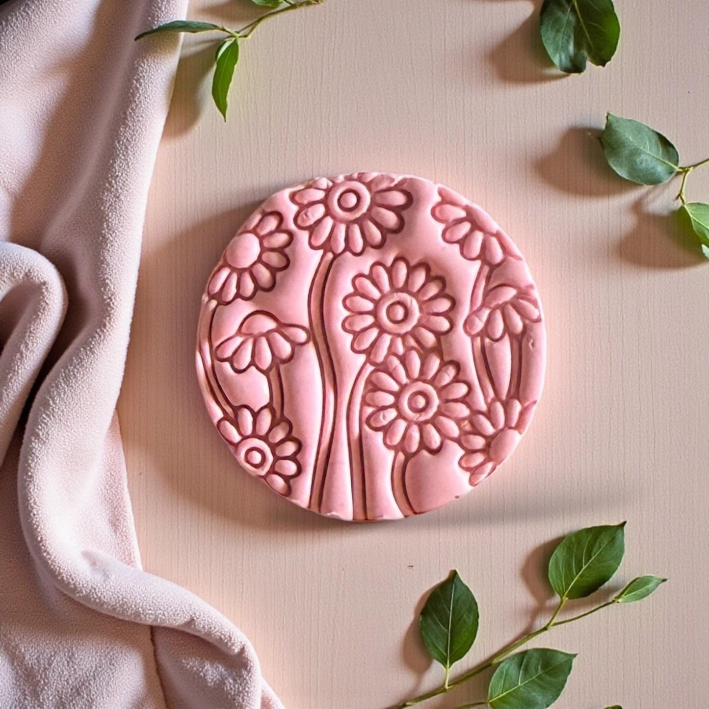 Pink daisy clay design surrounded by fabric and soft greenery