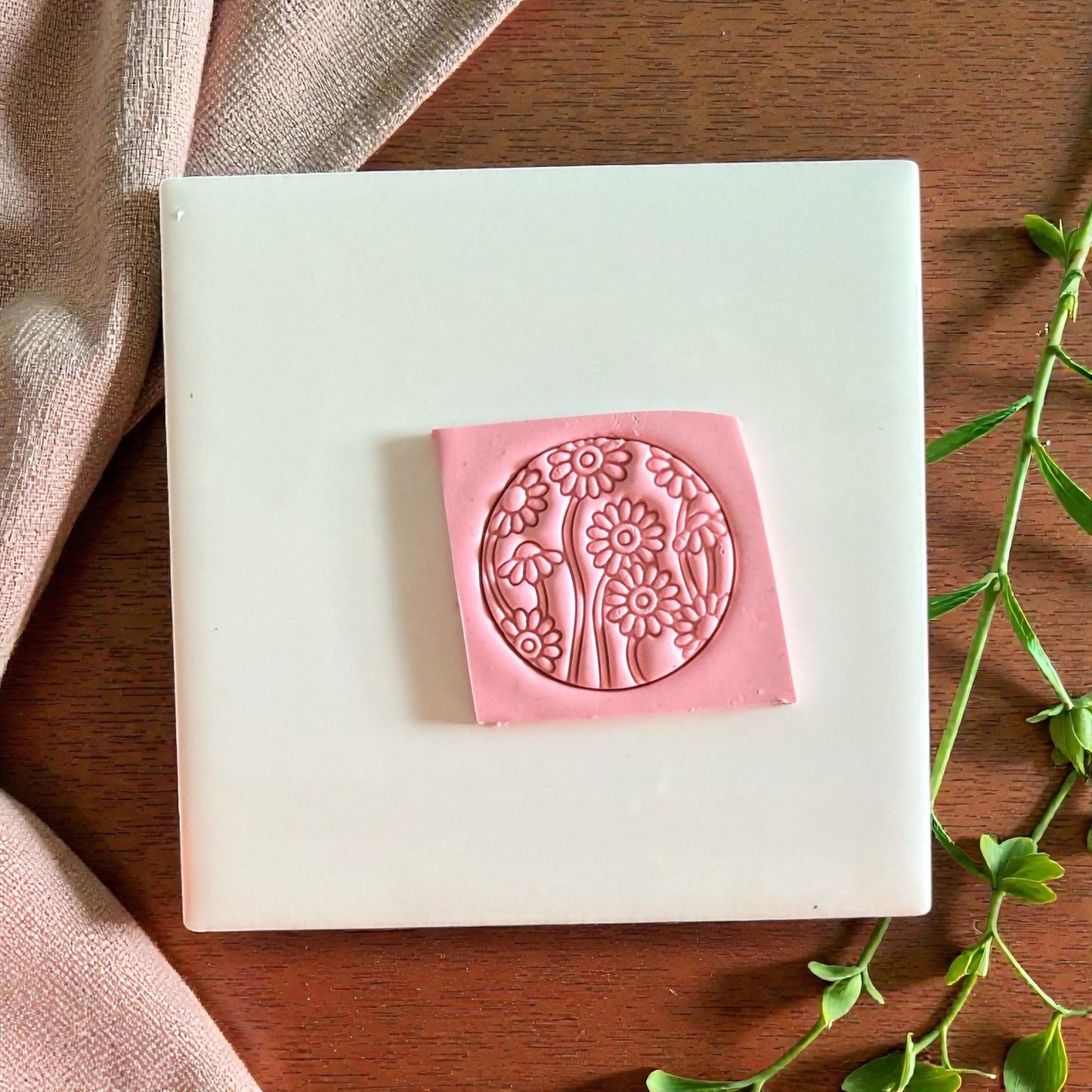 Pink round floral clay impression centered on tile with fabric and green leaves