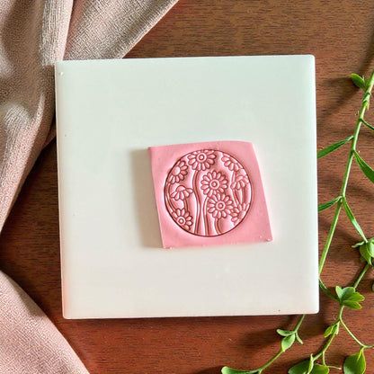 Pink round floral clay impression centered on tile with fabric and green leaves