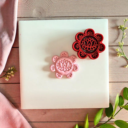 Red lotus cutter beside pink clay impression on white tile with greenery