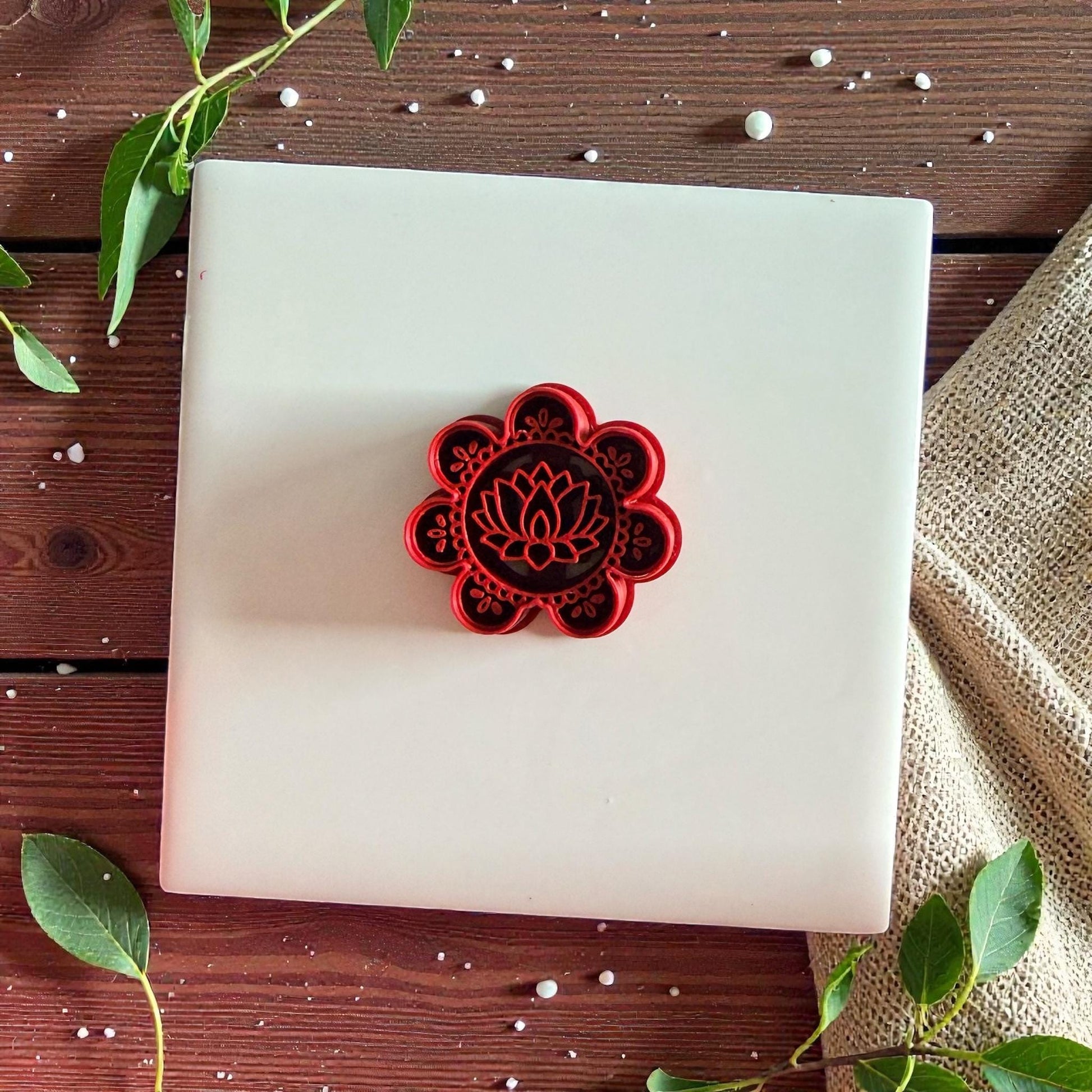Red lotus flower cutter centered on white tile with leaves and neutral fabric