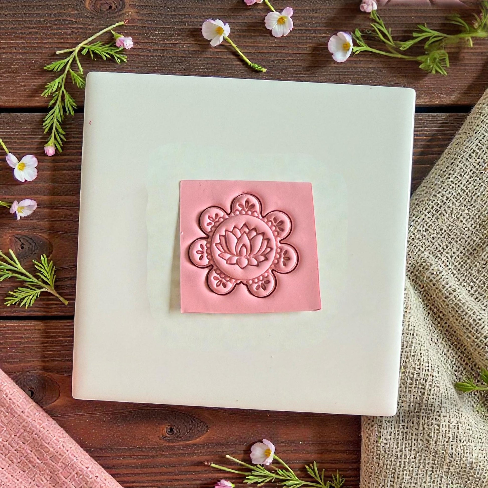 Pink lotus clay impression on white tile with greenery and flowers