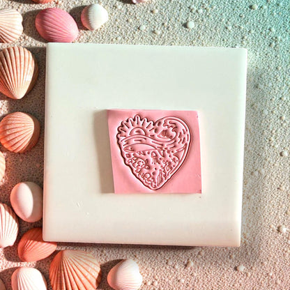 Pink ocean-inspired heart clay piece on sand with seashells