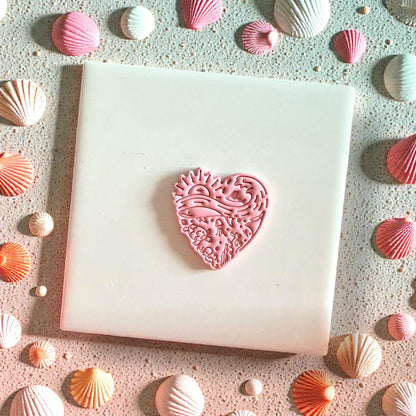 Pink heart clay design centered on tile surrounded by seashells