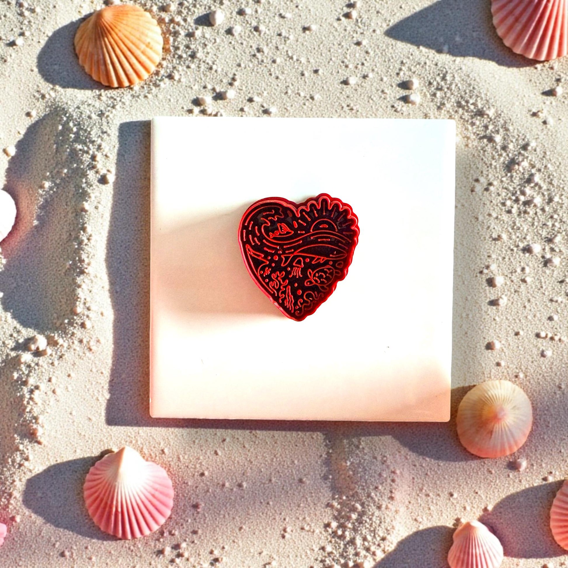 Close-up of red beach heart clay cutter with ocean design and shells