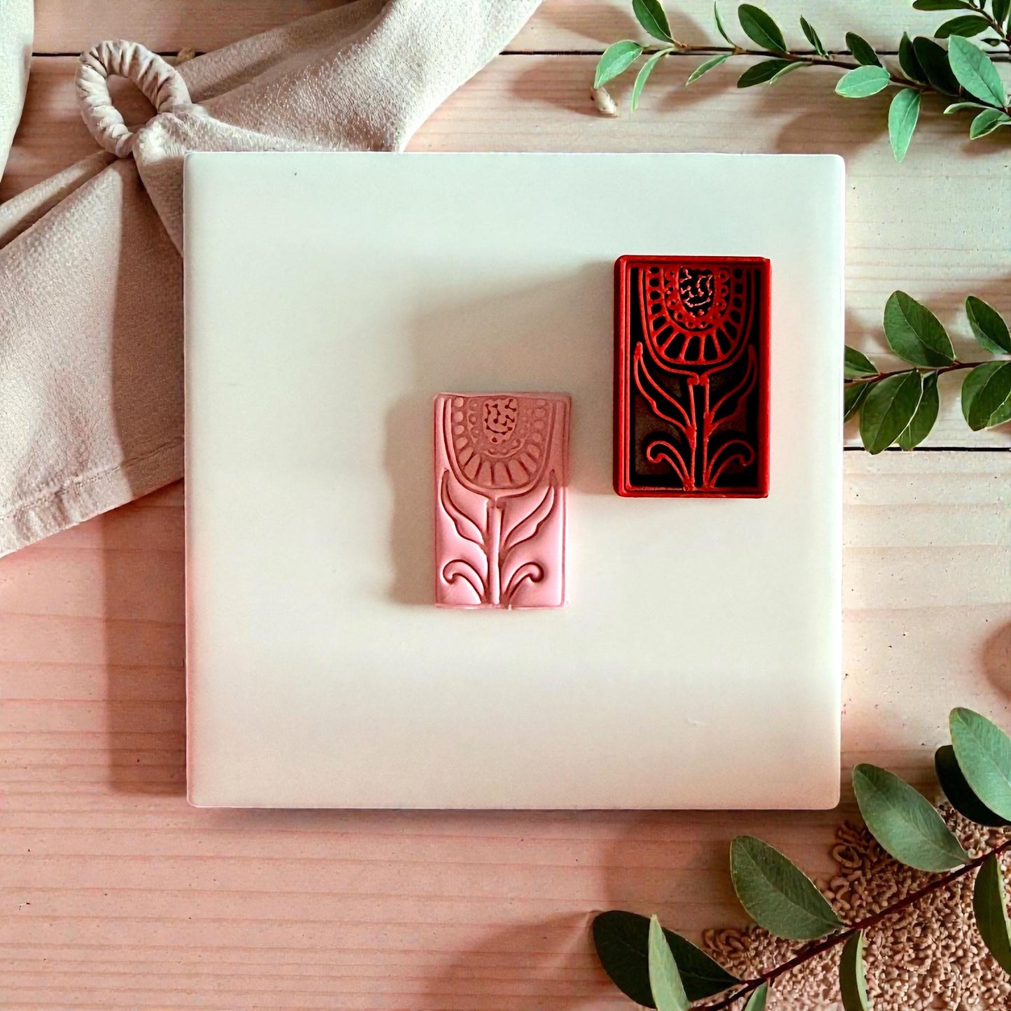 Pink clay impression beside red folk tulip cutter on wood tile with greenery