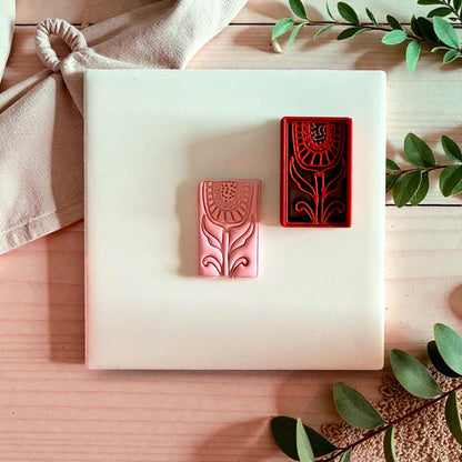 Pink clay impression beside red folk tulip cutter on wood tile with greenery