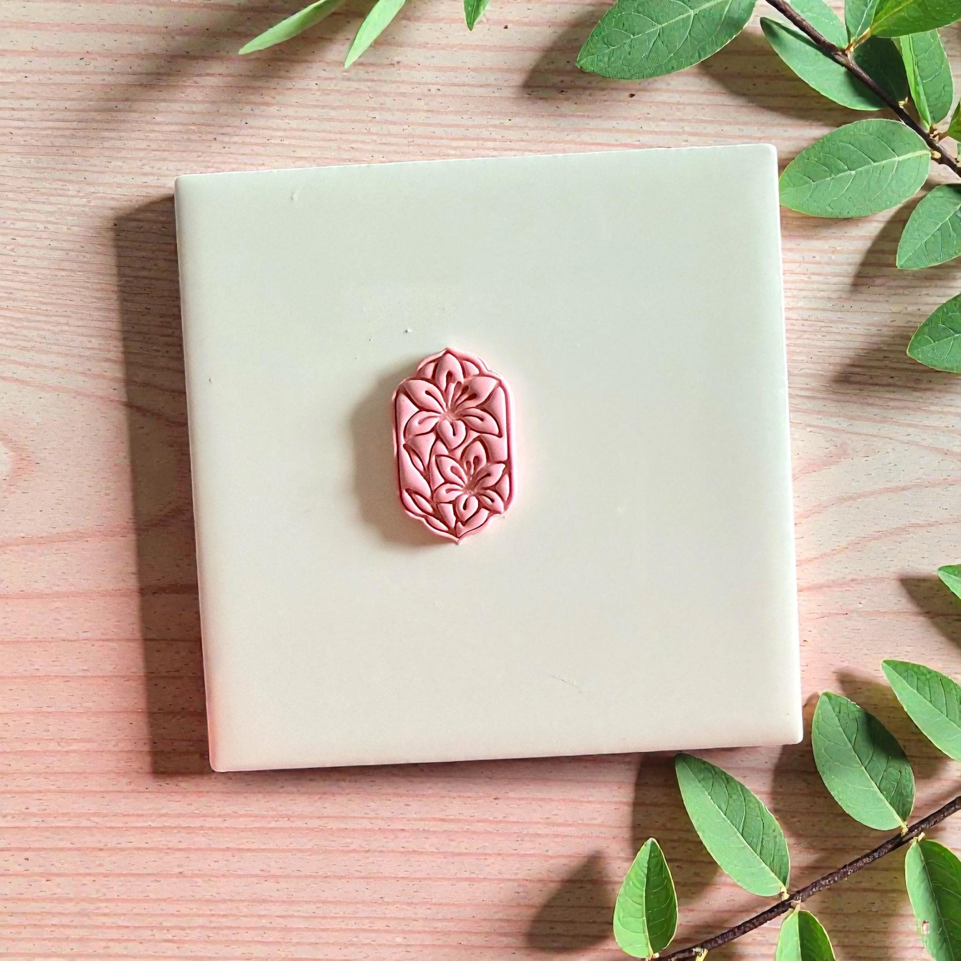 Pink ornate floral clay piece centered on tile with leaves