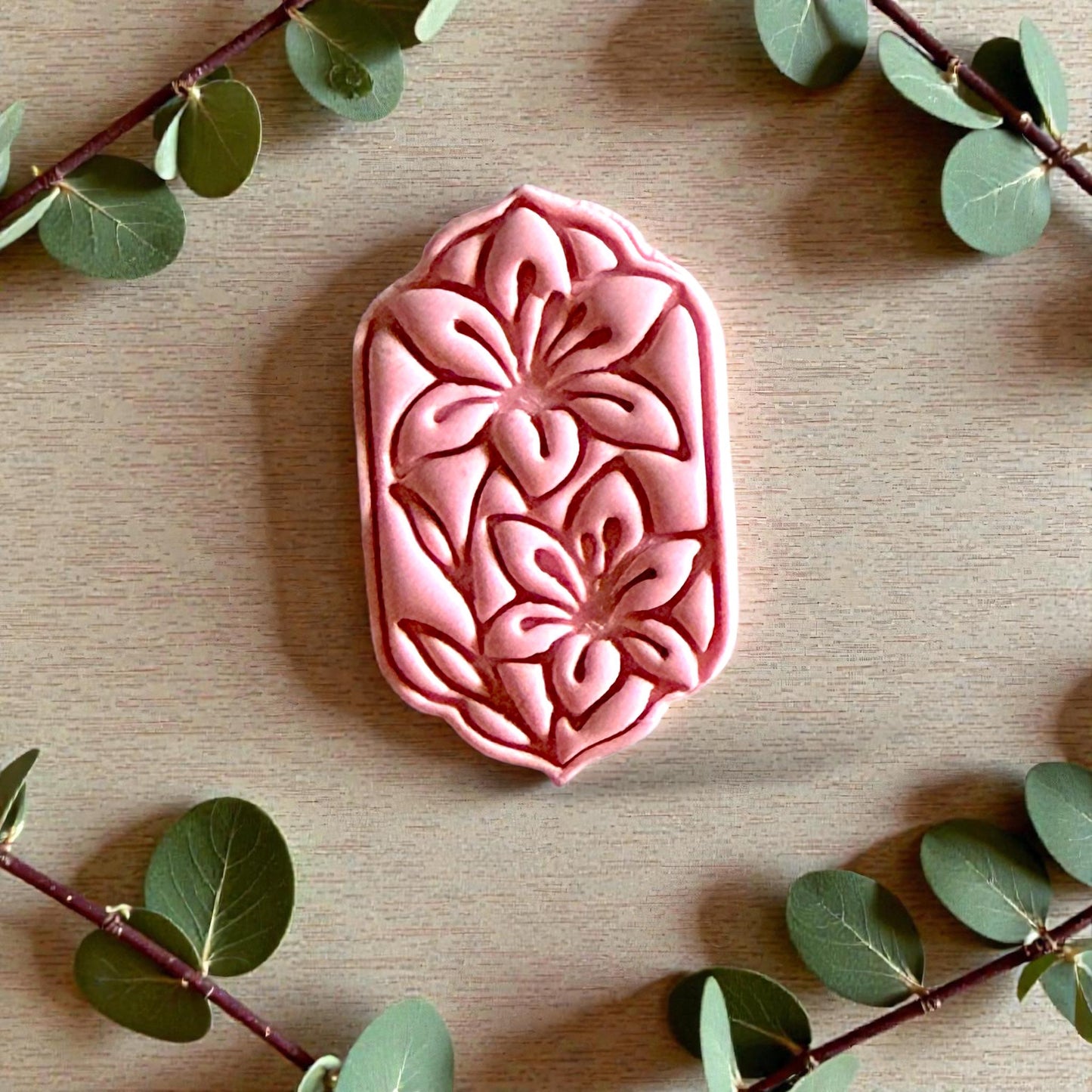 Pink floral clay design with two lilies surrounded by greenery