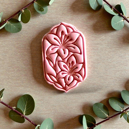 Pink floral clay design with two lilies surrounded by greenery