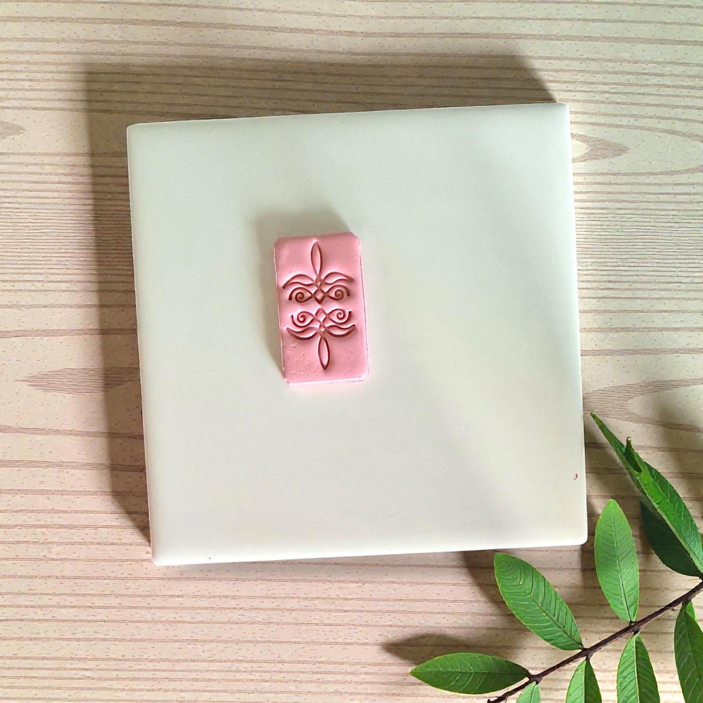 Pink clay rectangle with bootstitch design on white tile with leaves
