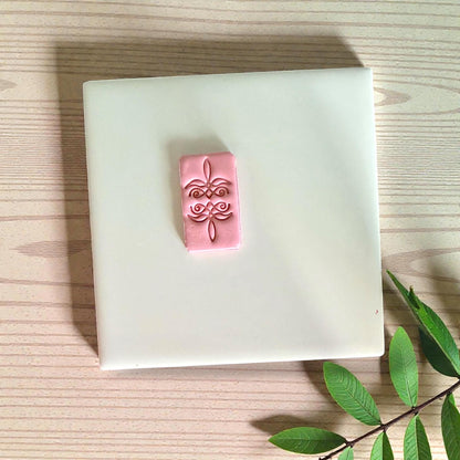 Pink clay rectangle with bootstitch design on white tile with leaves