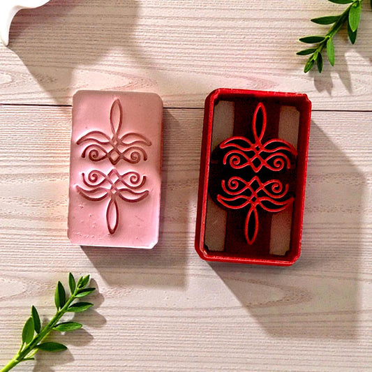 Pink clay imprint and red cutter side by side with green leaves