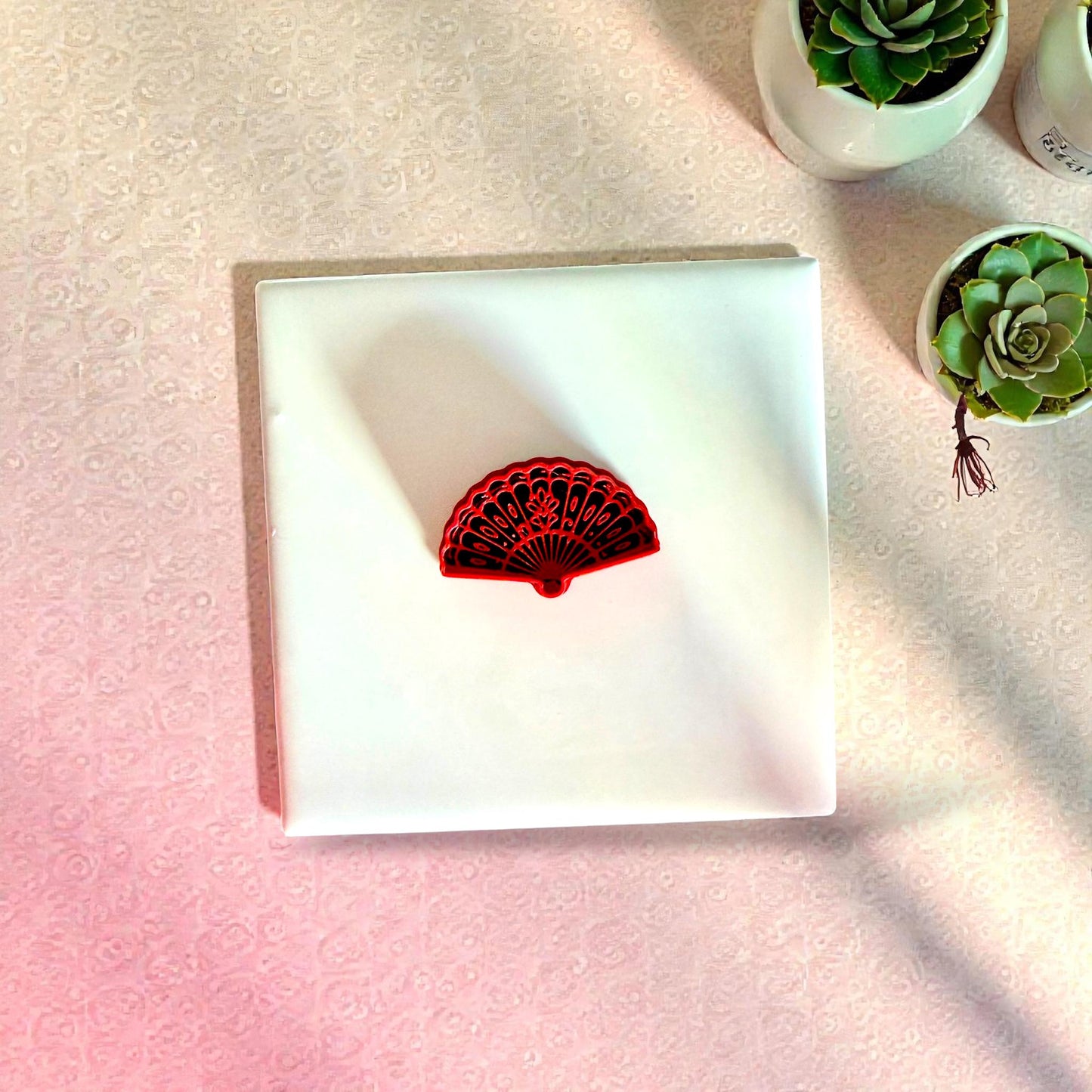 Red floral fan clay cutter on white tile surrounded by succulents