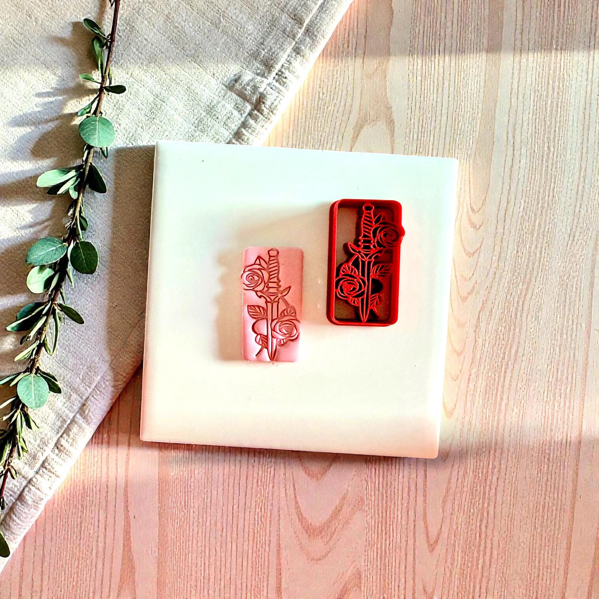Red dagger and rose polymer clay cutter next to pink clay impression on white tile