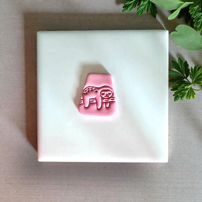 Pink sloth clay impression on white tile with greenery nearby