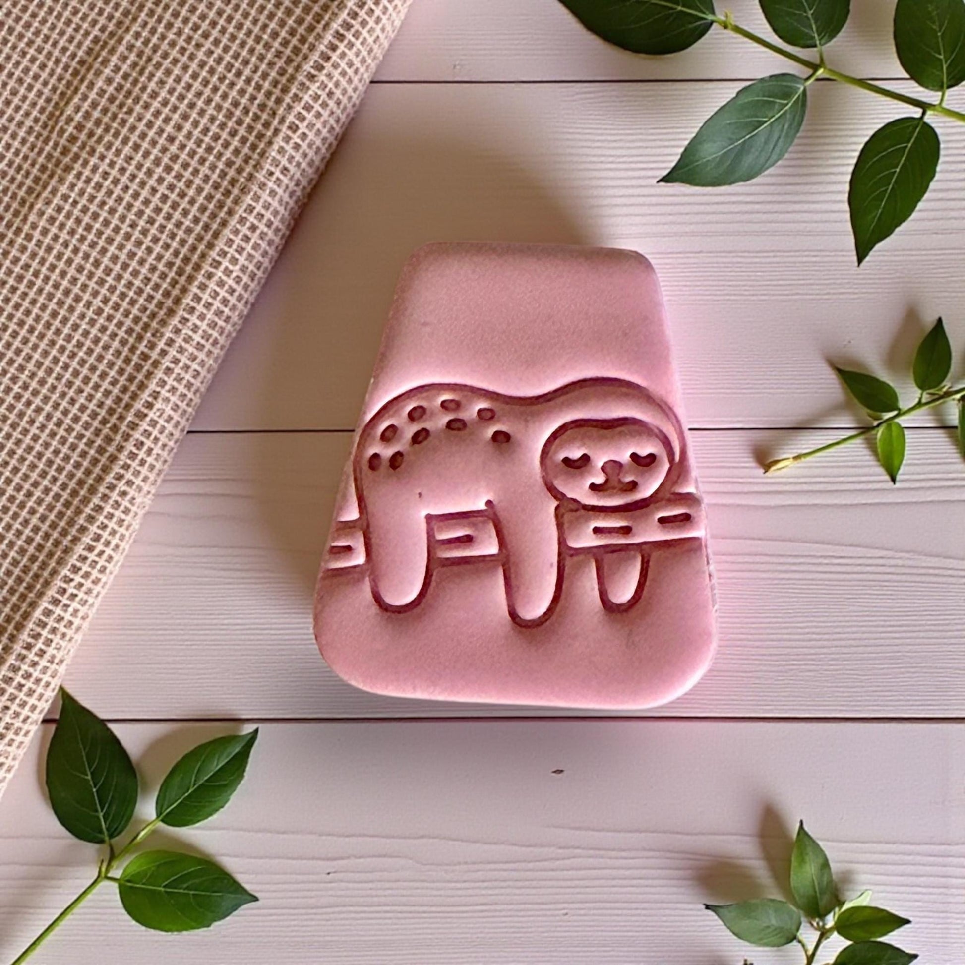 Pink clay sloth impression centered on white tile with leaves around