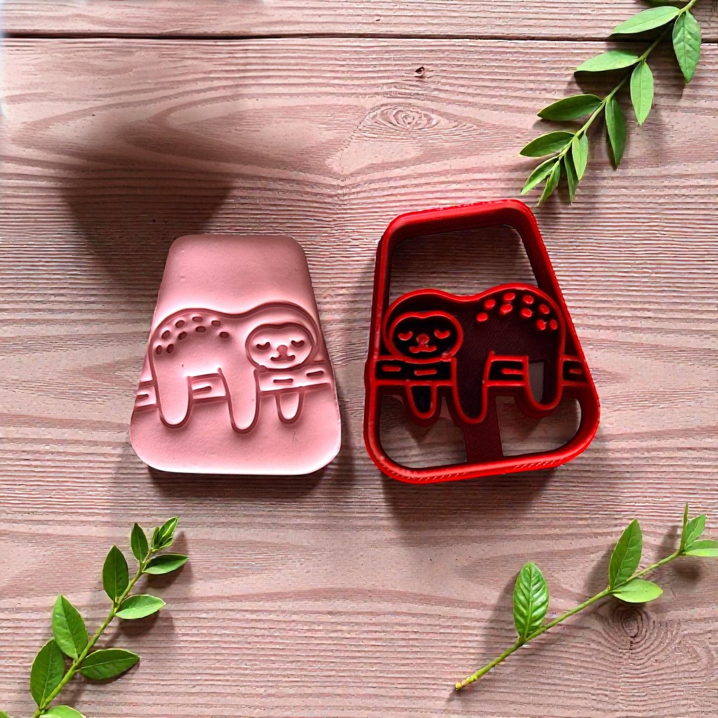 Pink and red sloth cutters side by side with greenery on wood surface