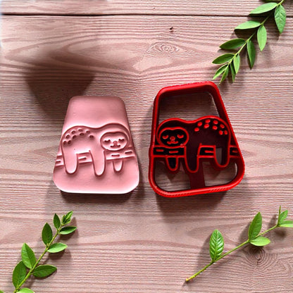 Pink and red sloth cutters side by side with greenery on wood surface