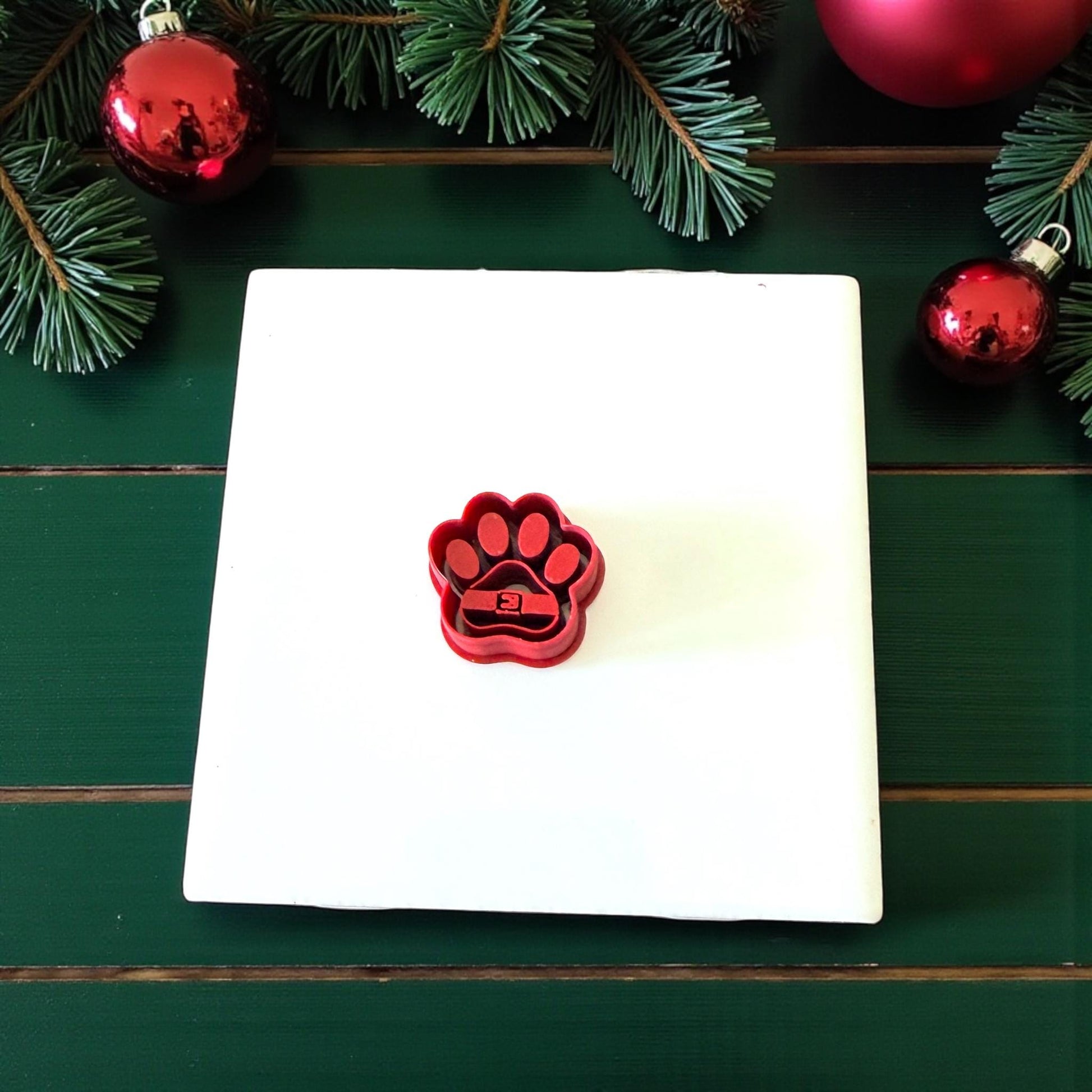 Red Santa paw clay cutter on white tile surrounded by holiday decor