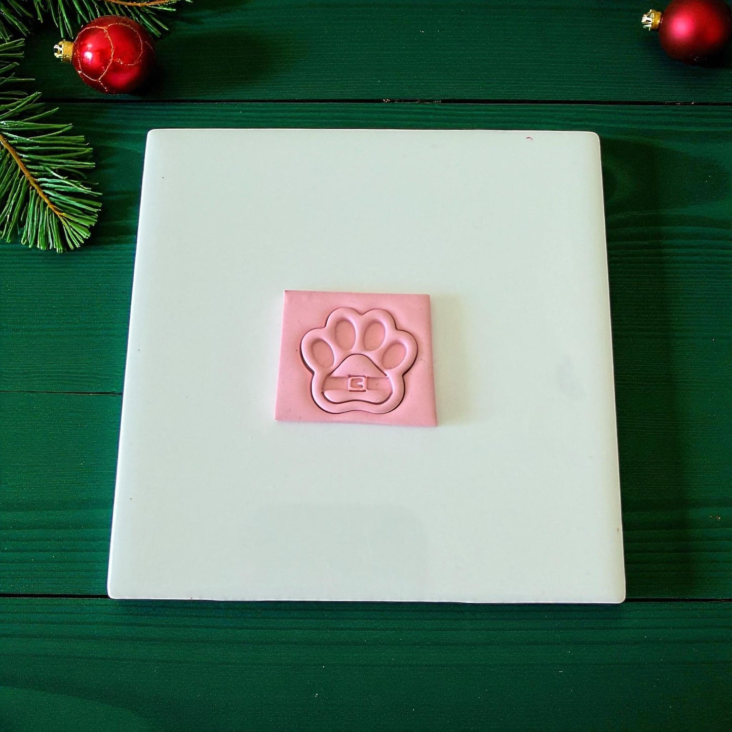 Pink Santa paw clay imprint on white tile surrounded by festive decor