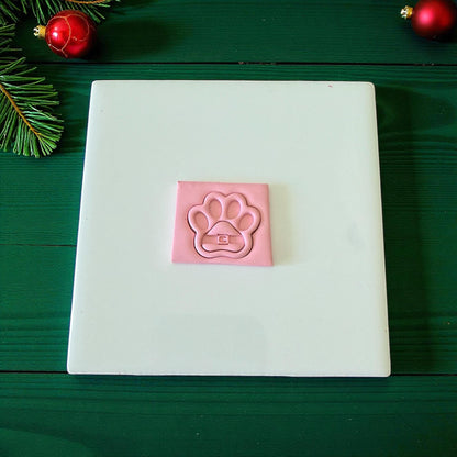 Pink Santa paw clay imprint on white tile surrounded by festive decor