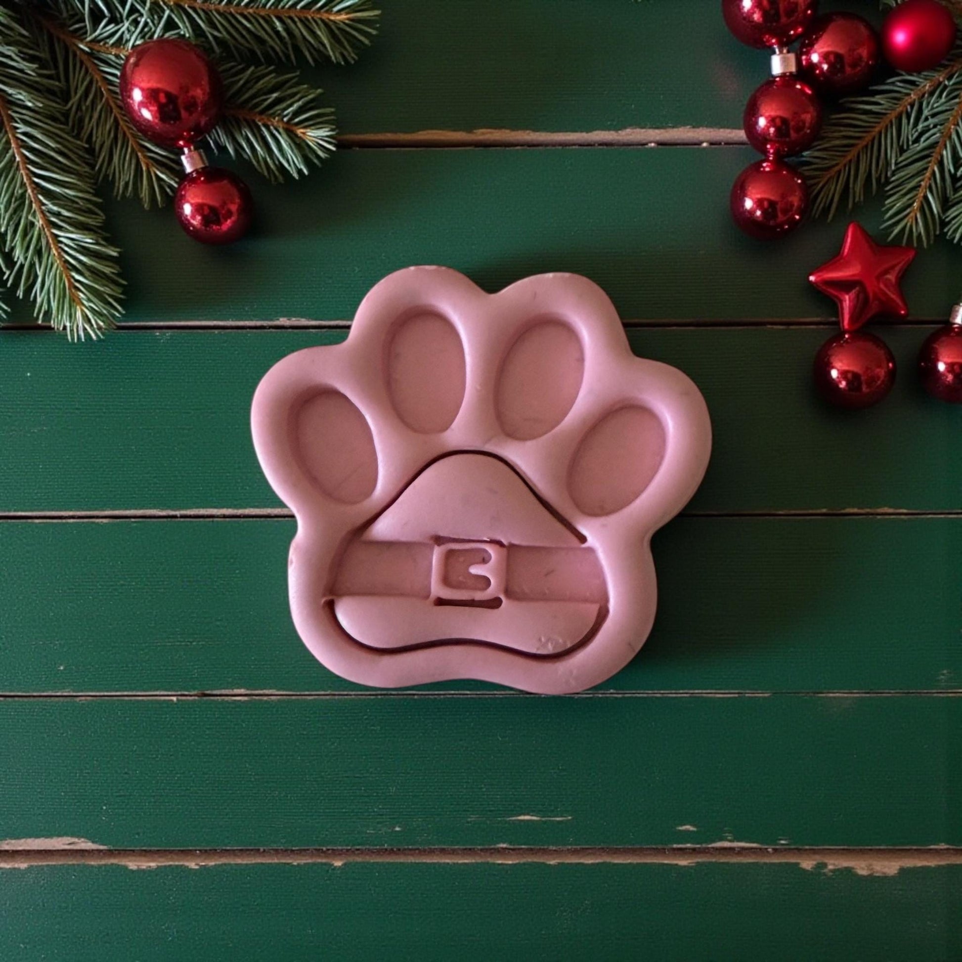 Pink Santa paw polymer clay cutter on green background with red ornaments