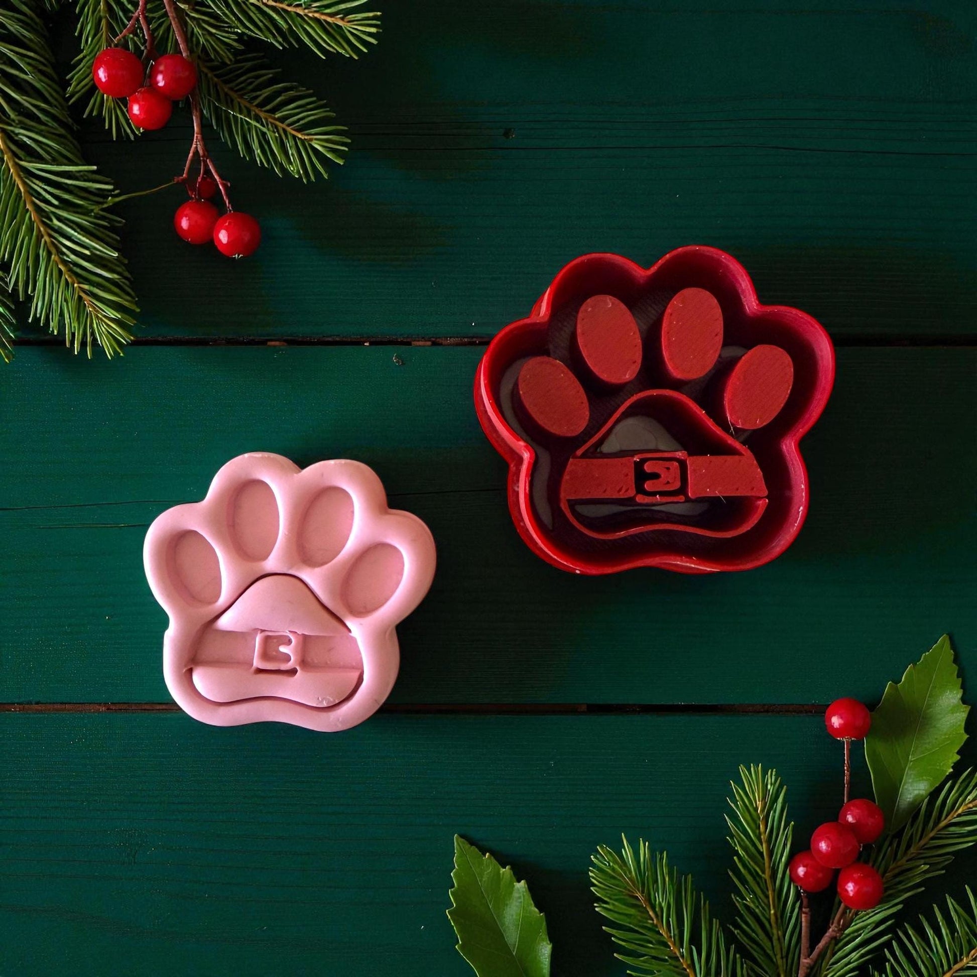 Pink and red Santa paw clay cutters on green background with holly and berries