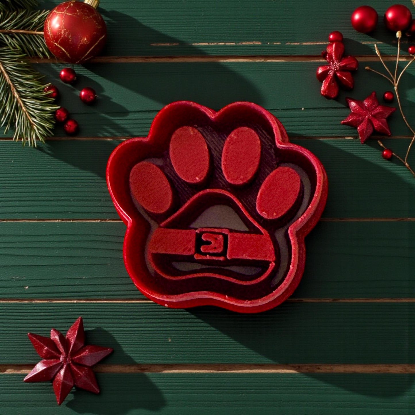 Red Santa paw polymer clay cutter on green background with ornaments