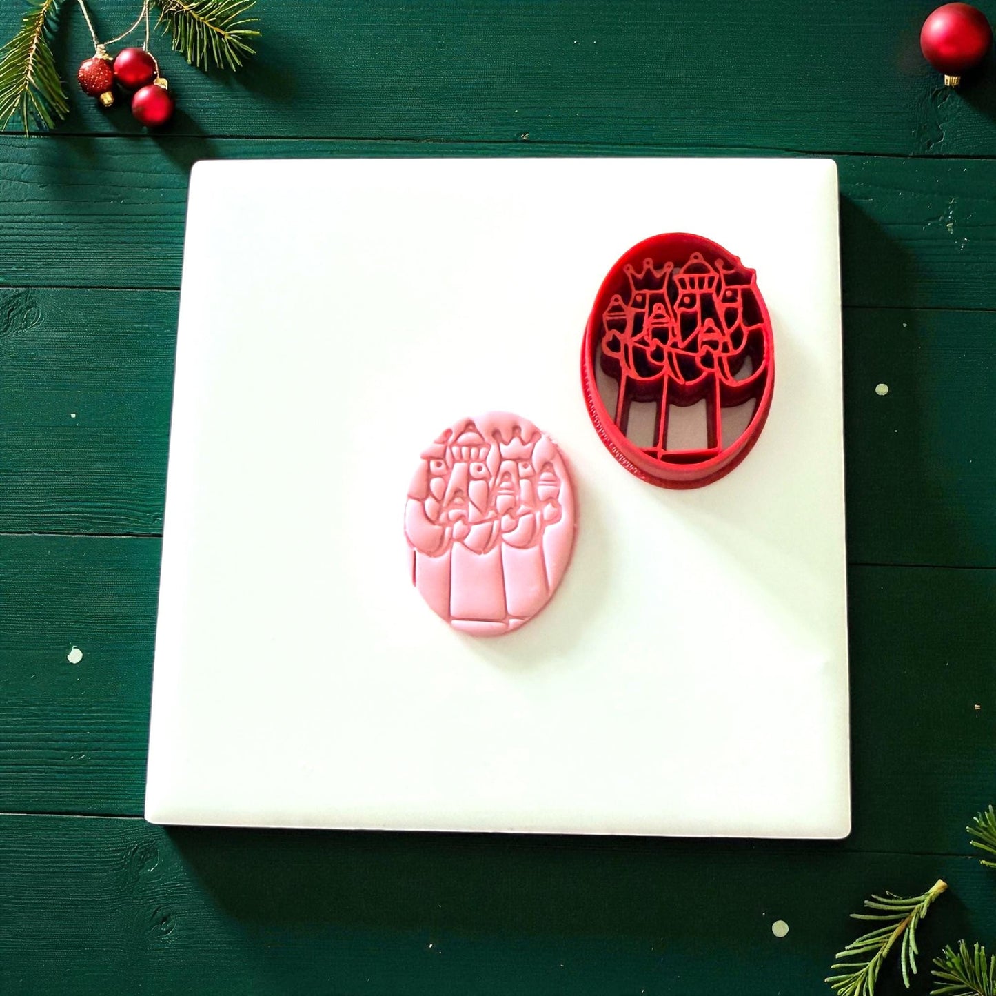 Pink and red Three Kings cutters on white tile with pine branches