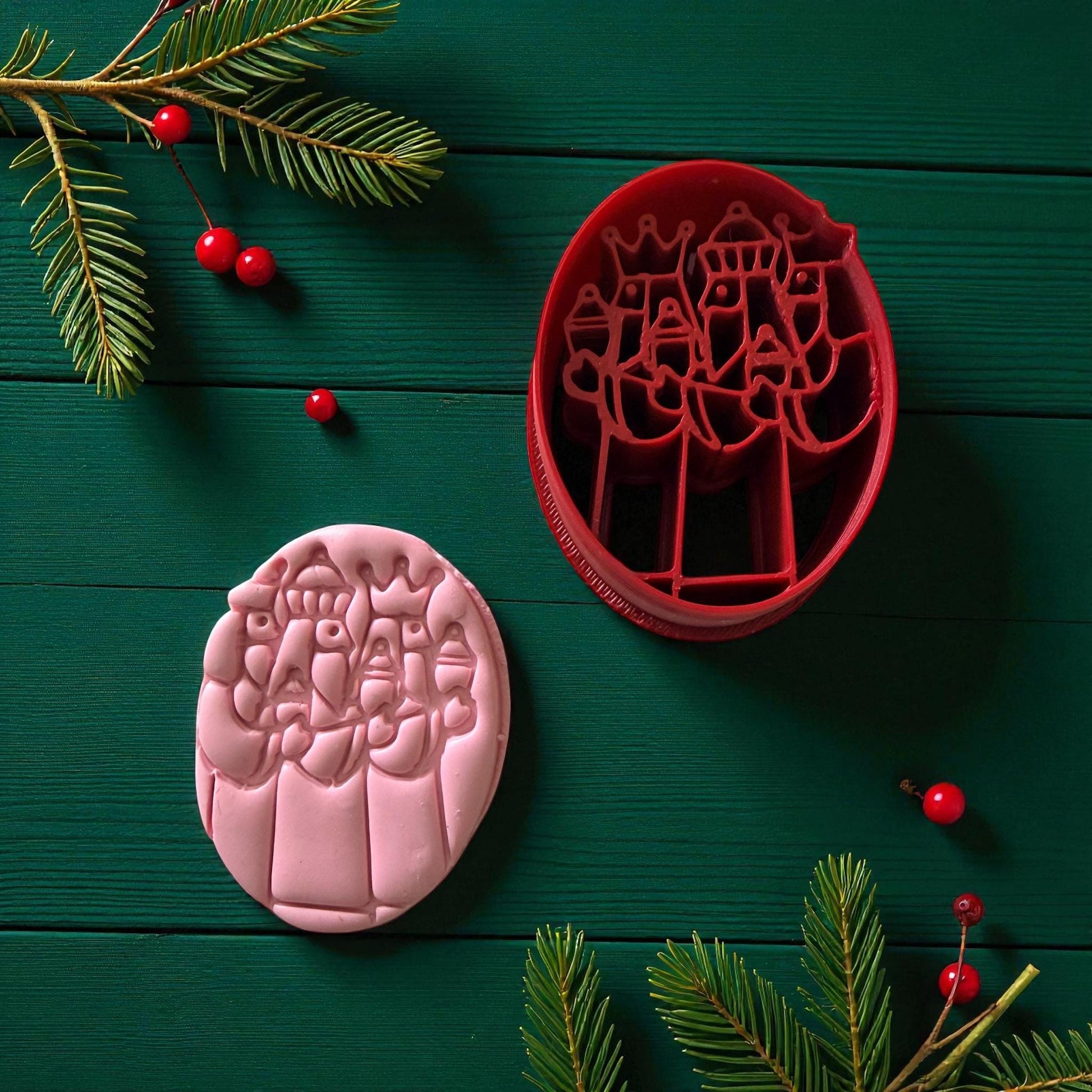Pink Three Kings clay imprint and red cutter on green background with berries