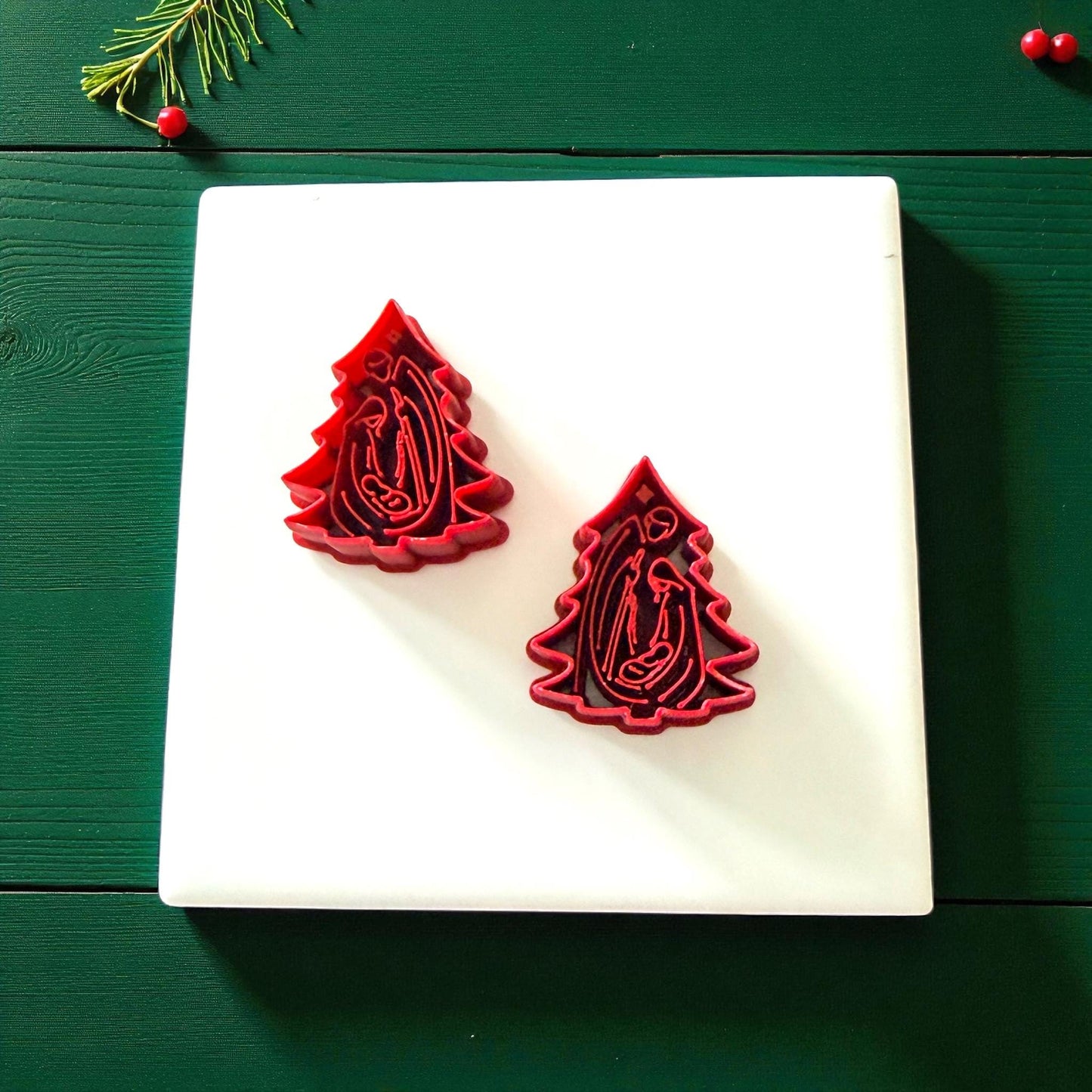 Pair of red nativity tree cutters on white tile with Christmas greenery